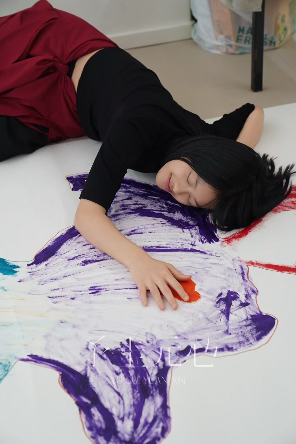 Joanna lying on a floor-wide painting, a brushstroke of purple paint beside her.